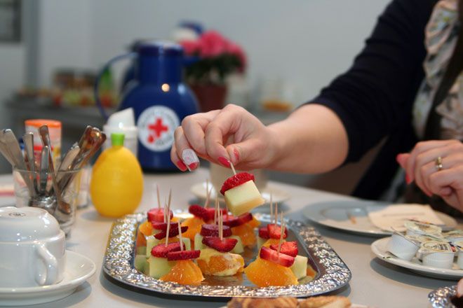 Foto: Eine DRK-Mitarbeiterin gießt die Balkonblumen in der Wohnung einer älteren Dame. Die ältere Dame wirkt glücklich und konzentriert sich mehr auf das gemeinsame Gespräch als auf die Blumen.