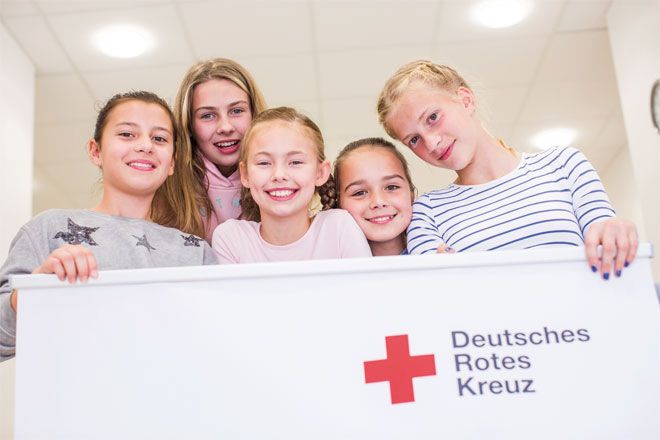 Foto: Mehrere Kinder halten ein DRK-Banner und blicken lachend in die Kamera.