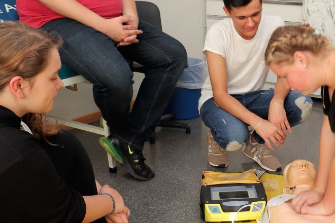 Foto: Eine DRK-Ausbilderin führt den Teilnehmern die Herzdruckmassage an einem Dummy vor.